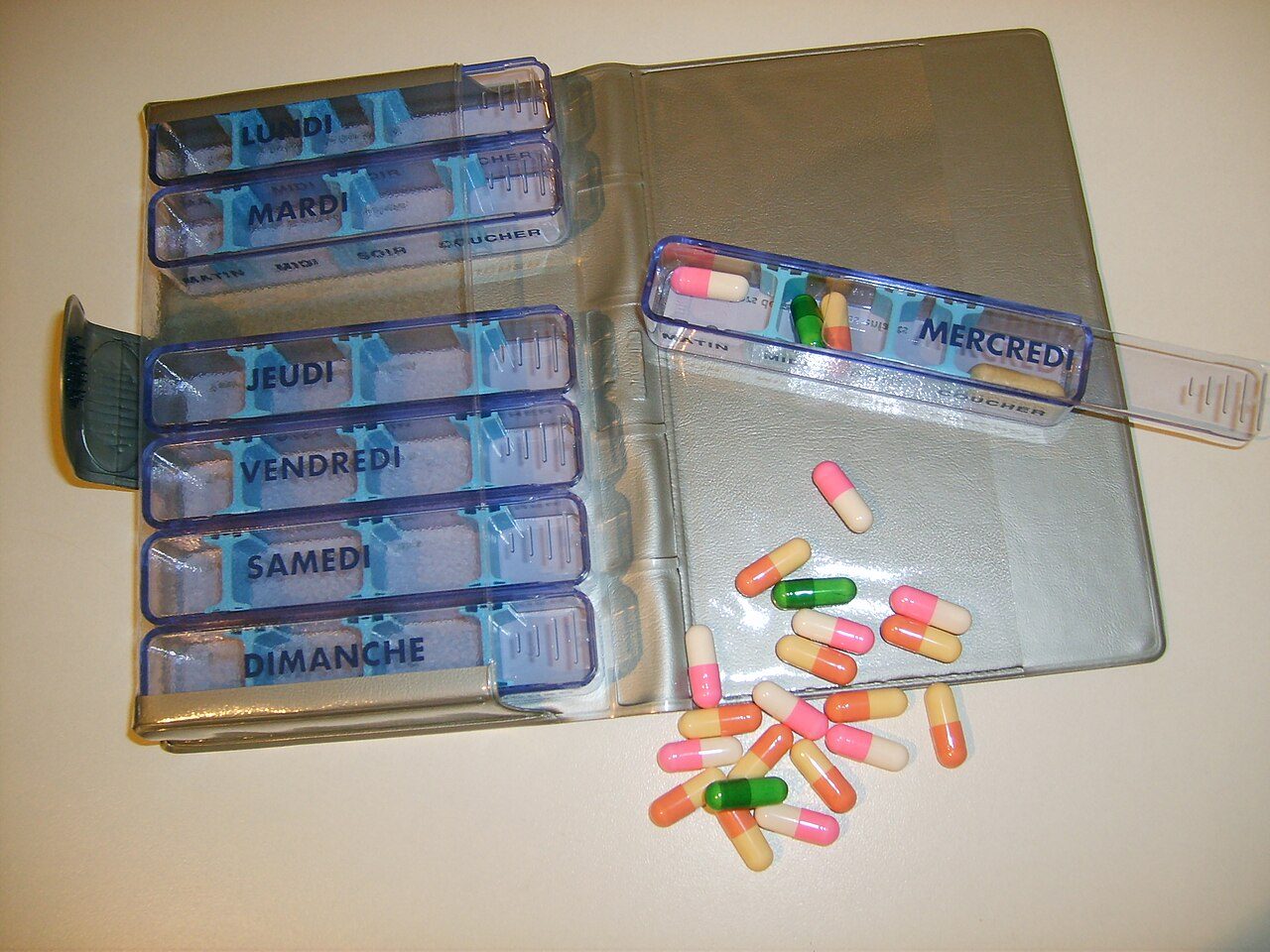 A weekly pill organizer with separate compartments and French day labels. The photograph does not identify the medicines.